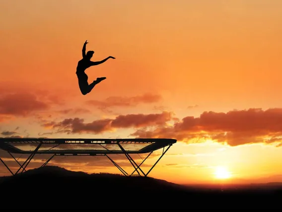 Woman jumping trampoline sunset