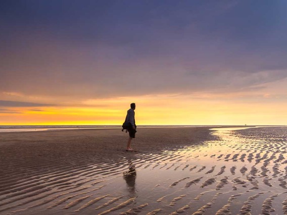 Man standing on beach at low tide during sunset